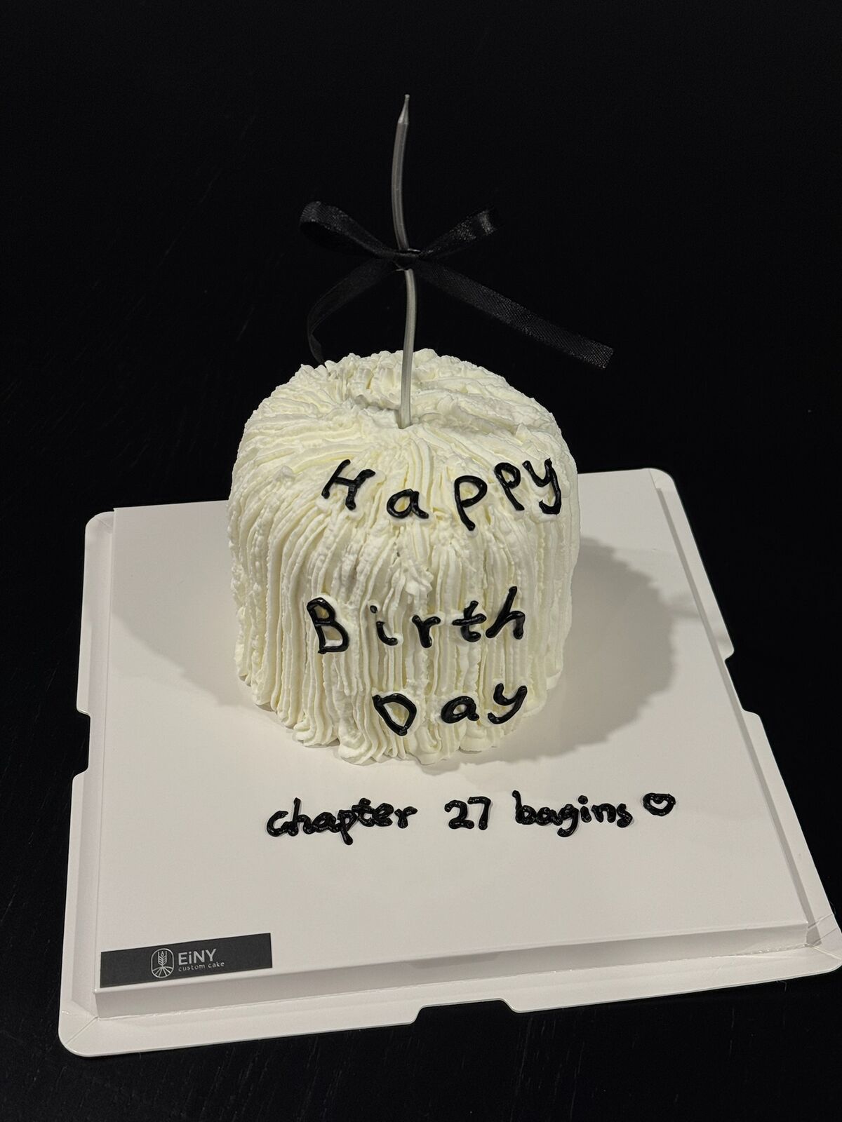 Tall ruffled white cake with a black bow and the words chapter 27 begins